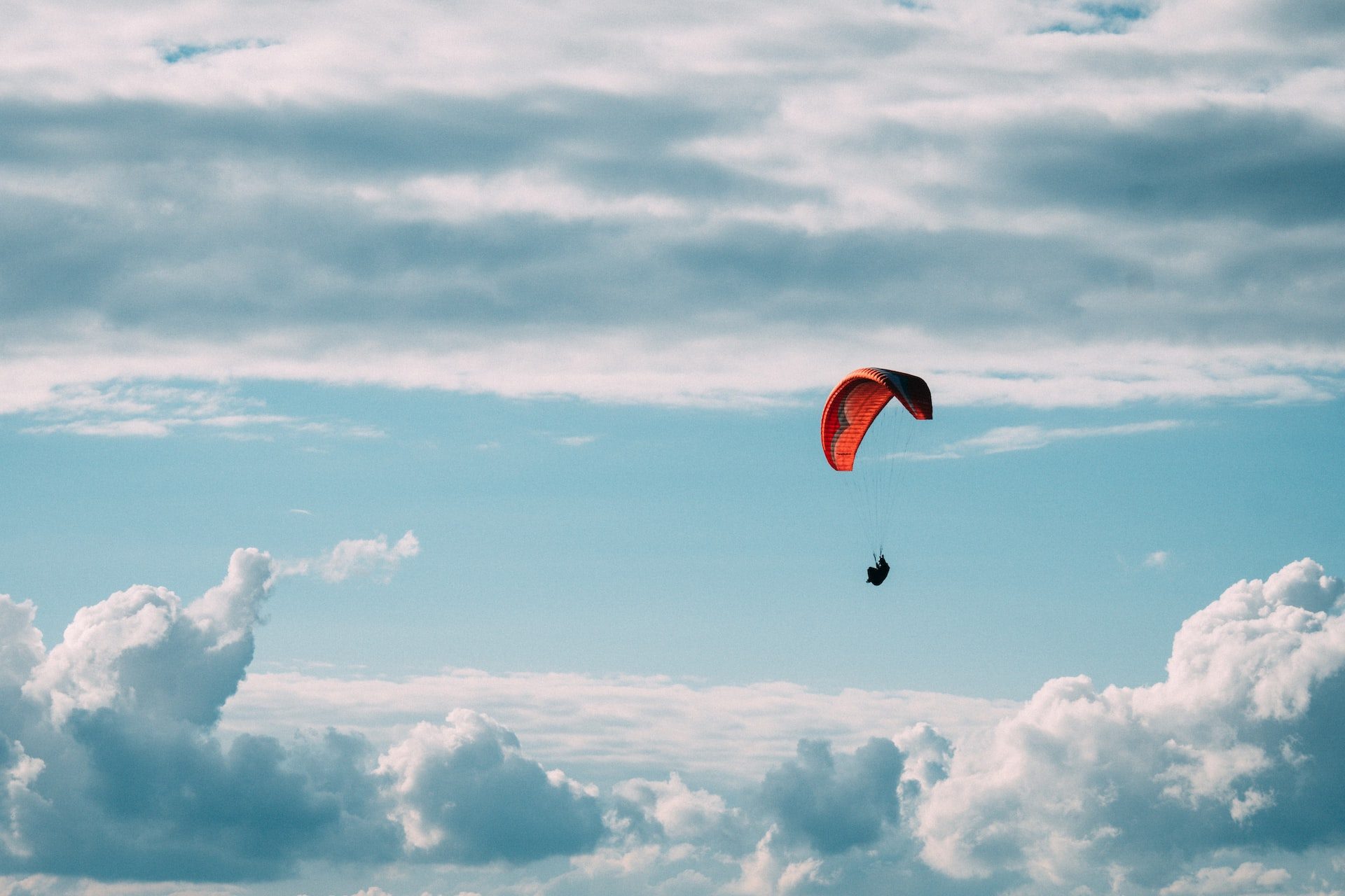 person in red parachute under white clouds during daytime
